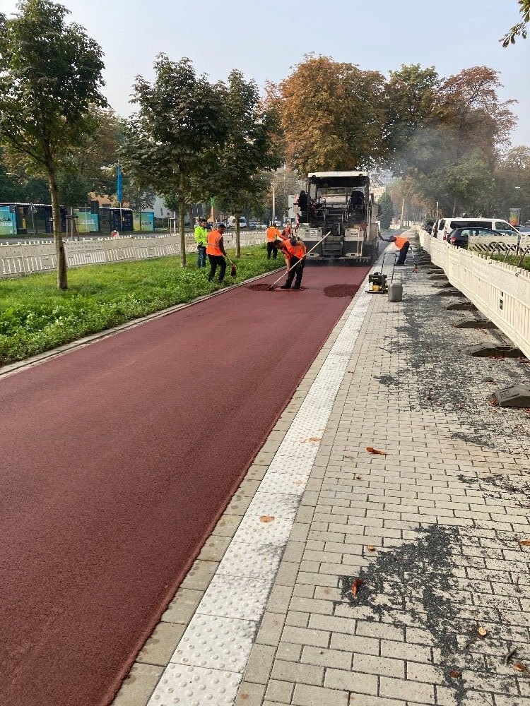 Mehrere Arbeiter und ein Baustellenfahrzeug asphaltieren den Radweg am Wall in Dortmund rot.