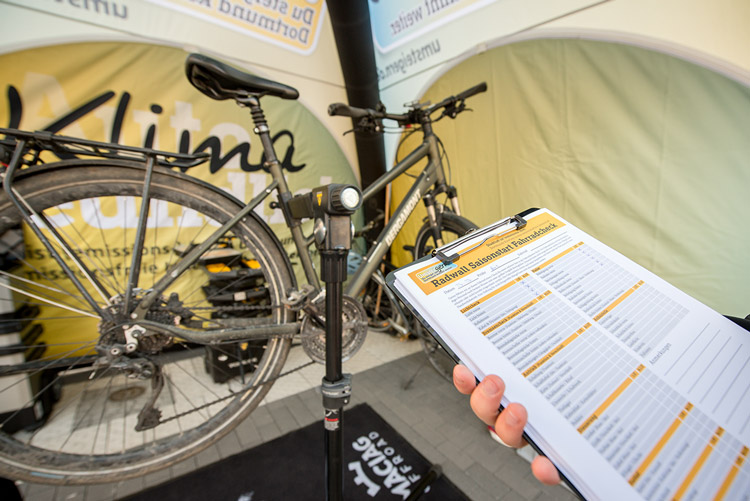 In einem UmsteiGERN-Zelt steht ein Fahrrad zum Check, im Vordergrund sieht man, wie eine Checkliste auf einem Klemmbrett gehalten wird. 